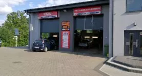 Widok na zewnątrz warsztatu Auto-Mar: jedno auto w trakcie naprawy, drugie wyjeżdża